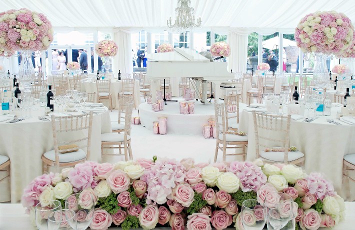 White Baby Grand Piano with Pink Hurricane Vases on a White Circular Stage Under a Crystal Chandelier – by The Angels